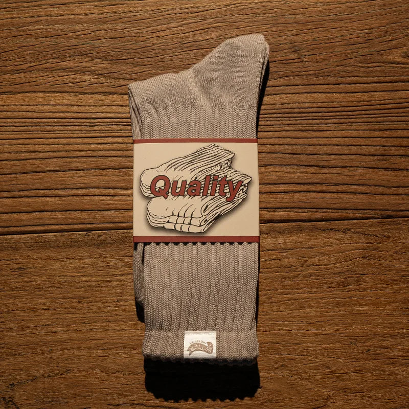 A pair of gray tube socks with a quality label featuring the word Quality on the front, resting on a wooden surface.