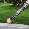 A person's arm is displayed with a black and white tattoo design of skulls, worn on a green lawn.