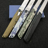 A precision folding pocket knife with a tan handle and a camouflage blade is displayed on a dark surface.