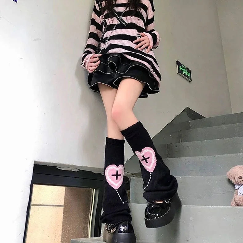 A person wearing black leg warmers with pink heart bows and a striped sweater and skirt is standing on stairs.