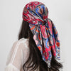 A woman wearing a vibrant red and blue paisley silk shawl scarf draped around her neck.