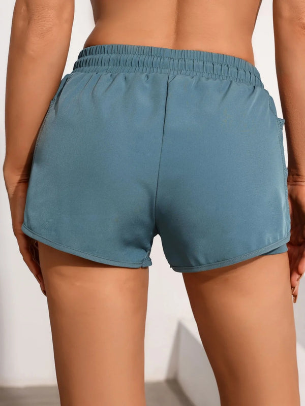 A close-up view of a teal athletic pair of shorts with mesh pockets worn by a model.