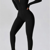 Model in black half-zip yoga jumpsuit and white sneakers.