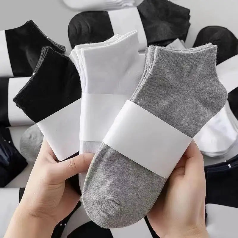 Una mano sostiene un calcetín gris con una banda blanca, rodeado de otros calcetines blanco y negro.