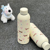 Taza térmica de acero inoxidable beige junto a un juguete pequeño para perro blanco.