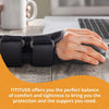 A hand wearing a black adjustable wrist support brace rests on a wooden table next to a laptop.