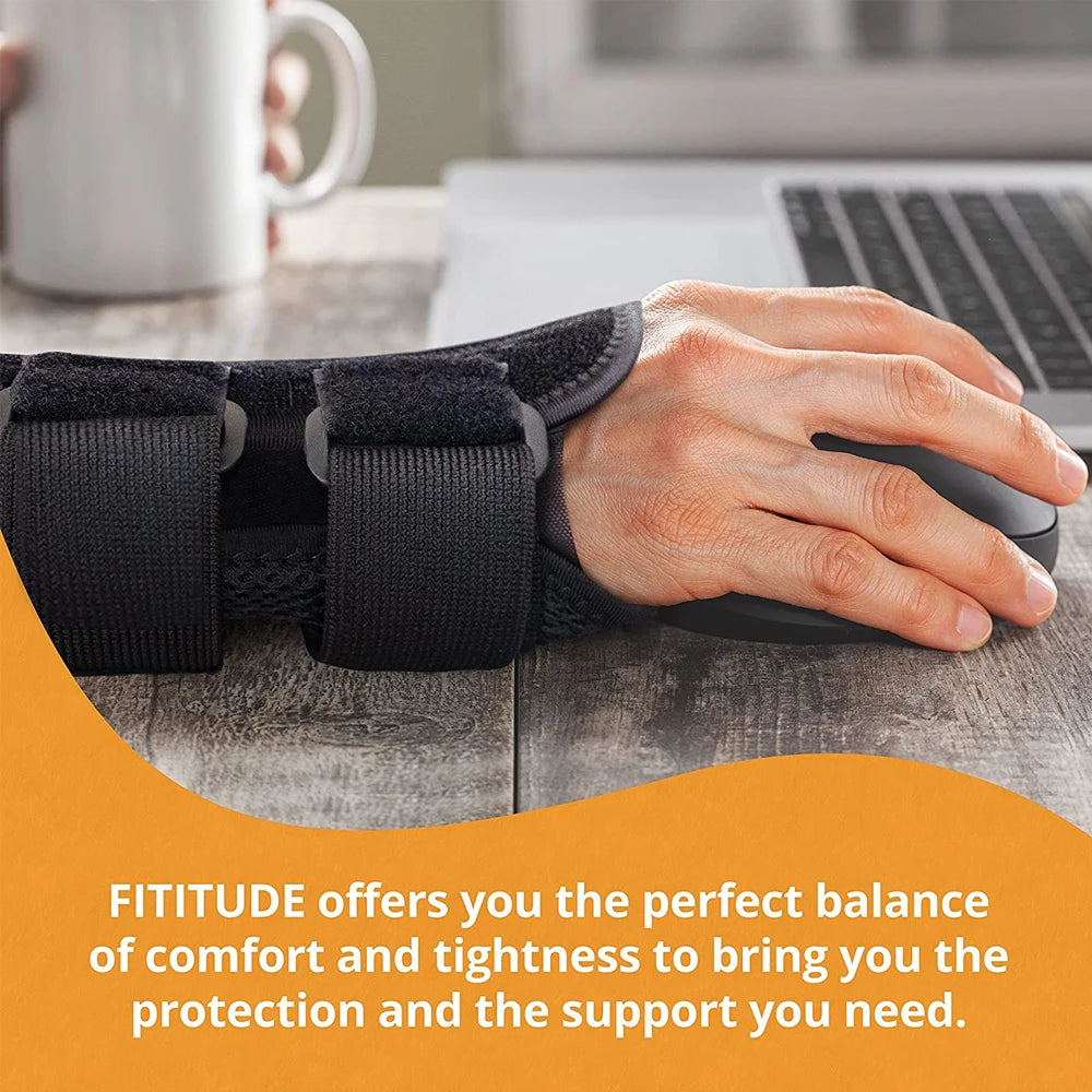 A hand wearing a black adjustable wrist support brace rests on a wooden table next to a laptop.