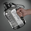 Eine Hand hält eine klare, große wiederverwendbare Sportflasche mit Messmarkierungen vor einem grauen Hintergrund.