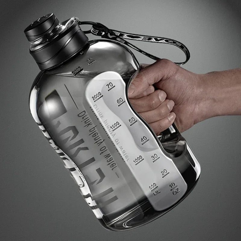 Eine Hand hält eine klare, große wiederverwendbare Sportflasche mit Messmarkierungen vor einem grauen Hintergrund.