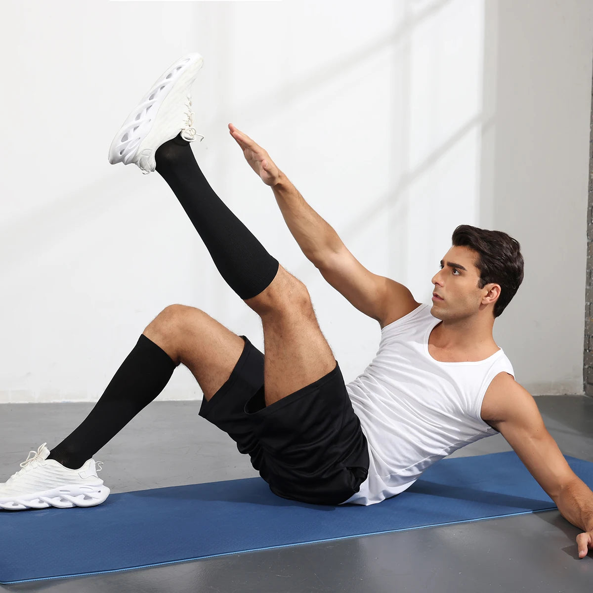 A man wearing white compression socks is performing a yoga pose on a blue mat.
