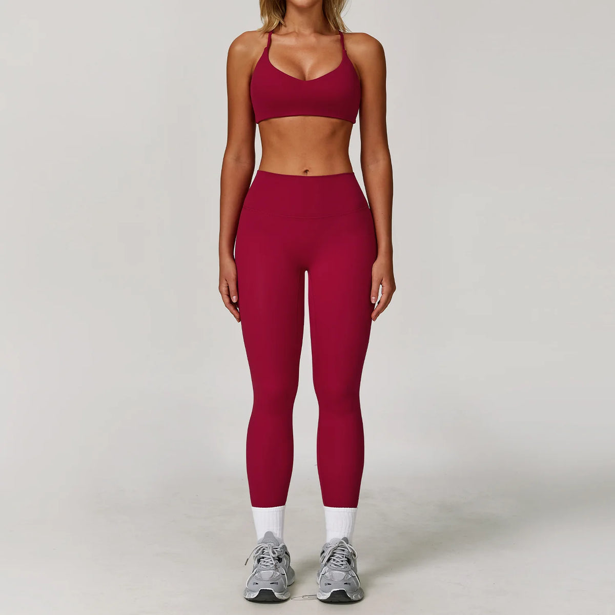 A woman models a maroon 3-piece yoga sports set consisting of a cropped top, leggings, and a sports bra.