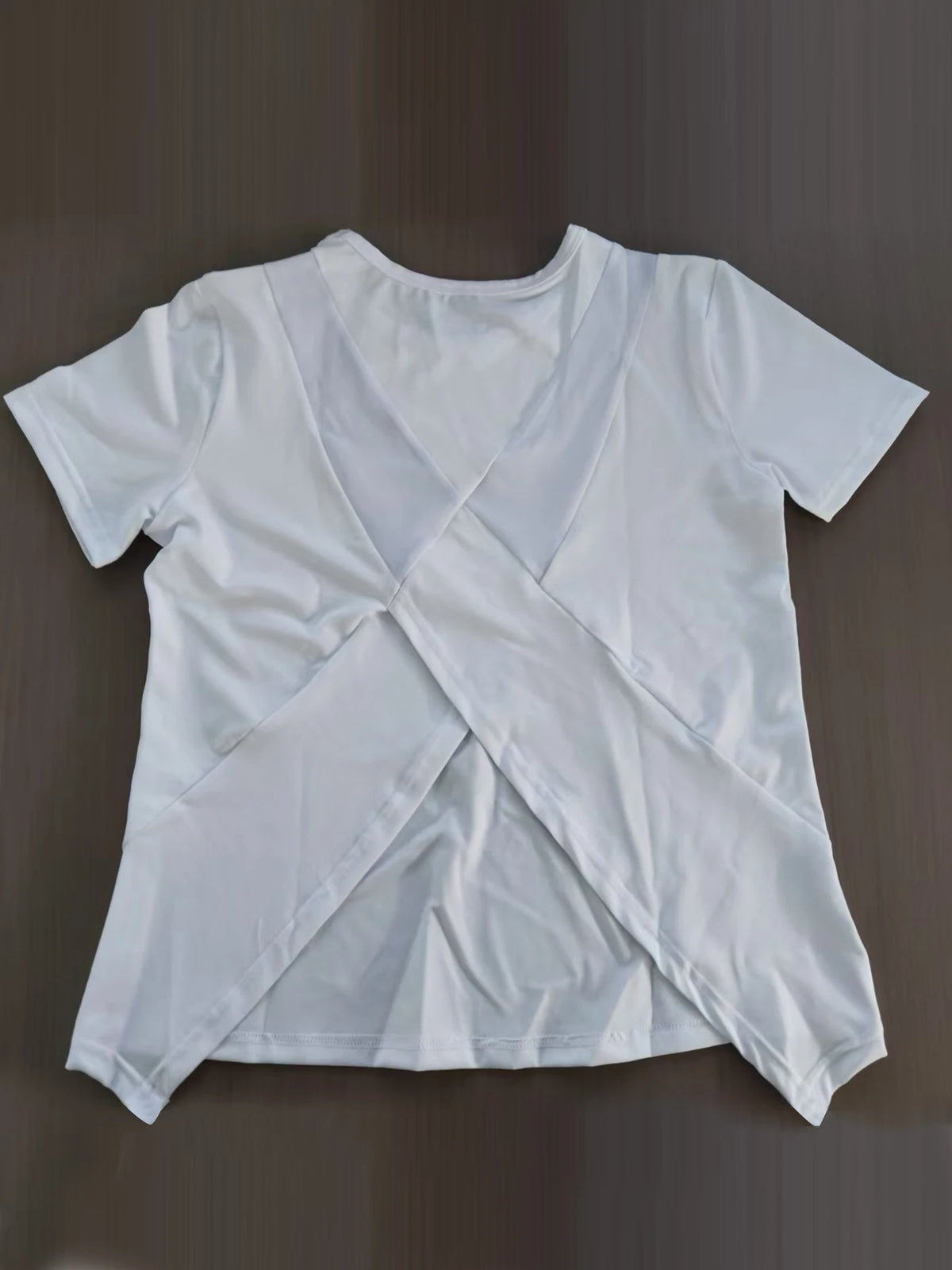 White women's breathable summer yoga and fitness t-shirt folded on a dark surface.