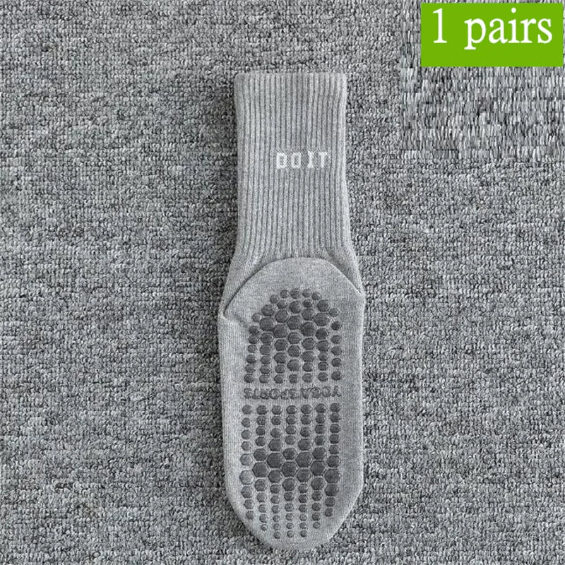 Ein Paar grauer atmungsaktiver, rutschfester Yoga- und Fitnesssocken, flach auf strukturiertem grauem Stoff.