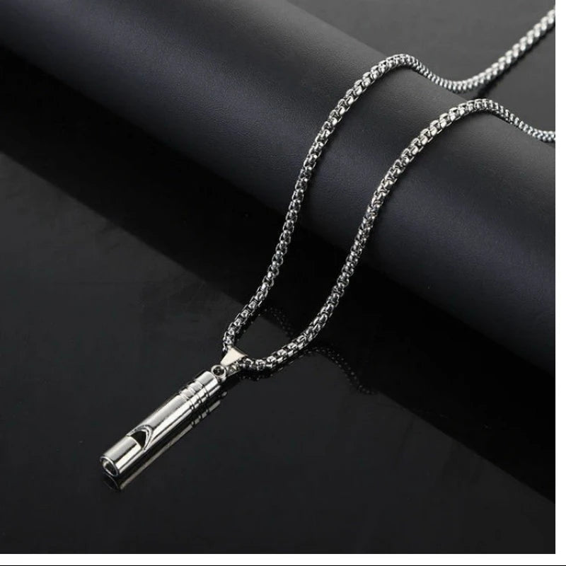 A silver stainless steel whistle pendant necklace with a chain is displayed against a dark background.