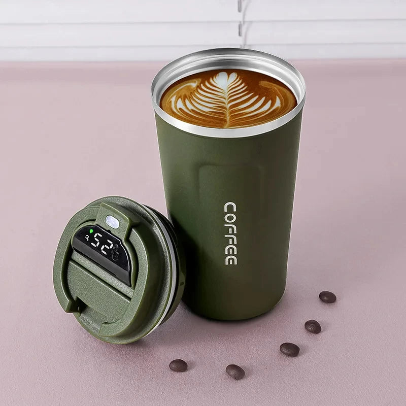 A dark green insulated thermos bottle with a lid is shown next to a cup of latte art on a pink surface.