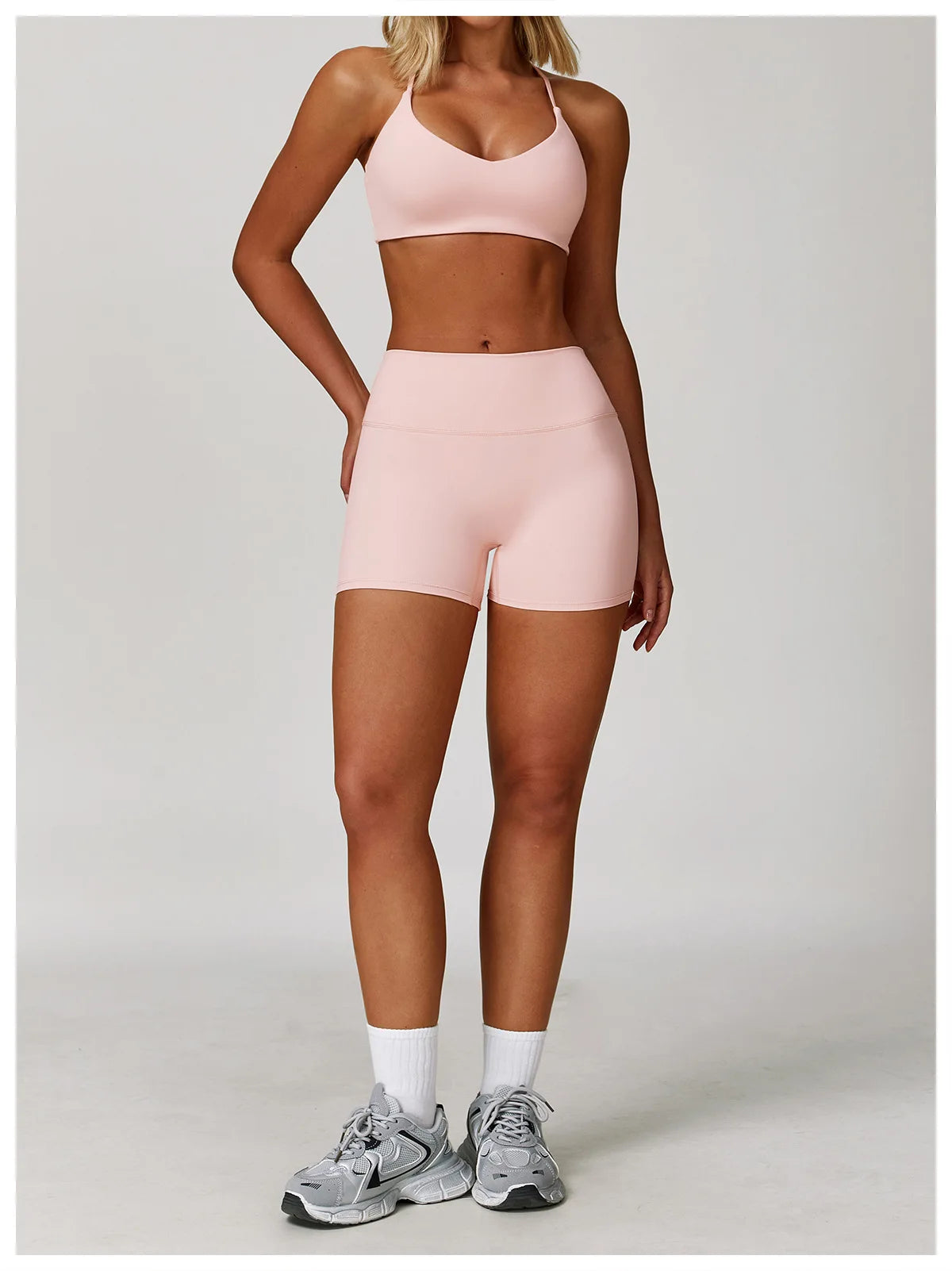 A woman models a pink 3-piece yoga sports set consisting of a crop top, brief, and shorts.