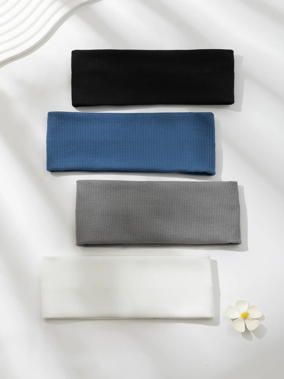 Un paquete de cuatro bandas elásticas para el cabello en negro, azul, gris y blanco, sobre una superficie blanca.