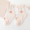 A pair of light pink knitted baby socks with small orange floral embroidery are displayed on a white surface.