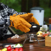 A hand wearing orange leather welding gloves is operating a small electric grinder on a wooden table.