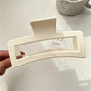A close-up of a white matte claw clip is held against a white background.