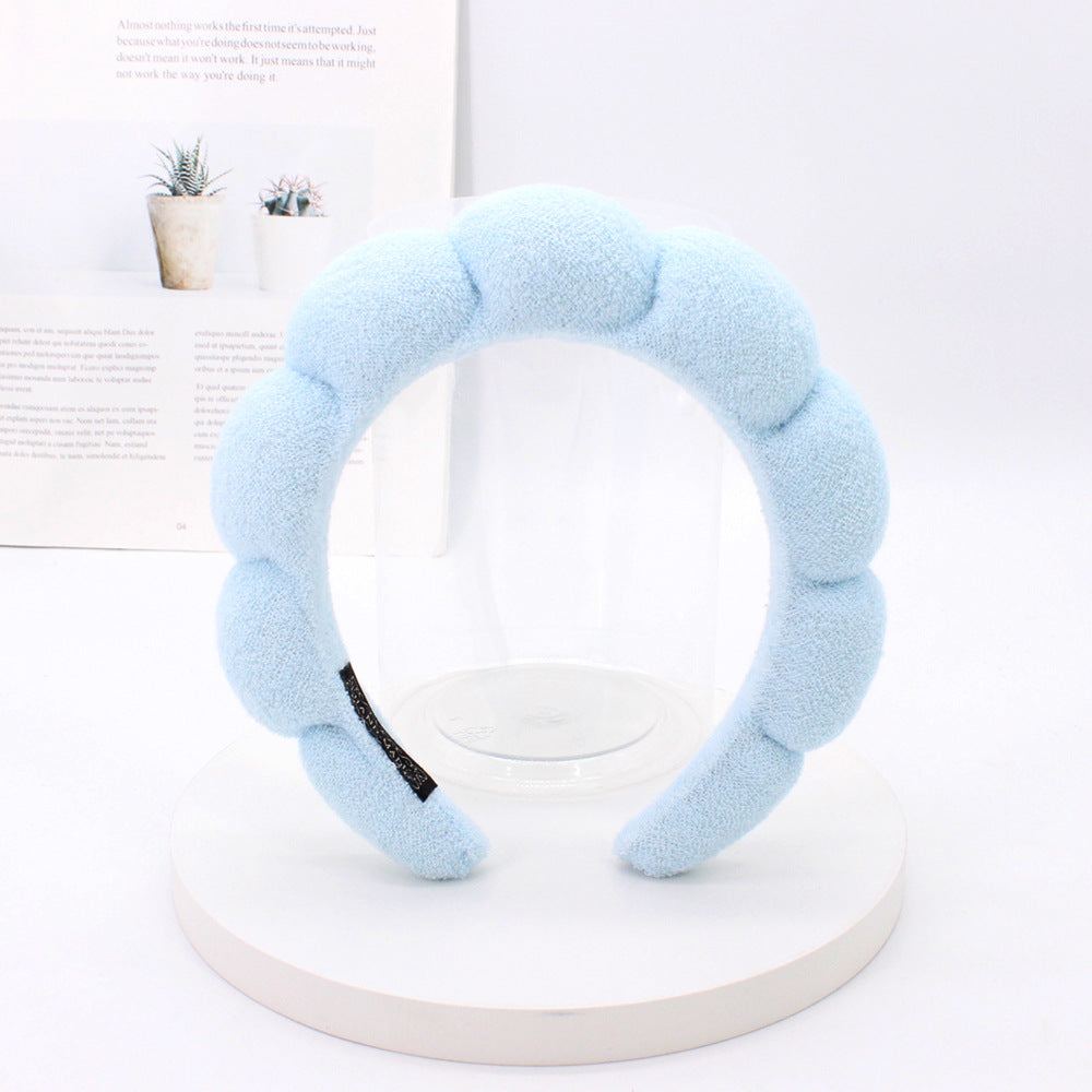 Light blue sponge terry cloth headband for hair styling displayed on a white stand.