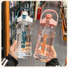A hand holds a clear insulated sports water bottle with a pink lid and straw against a blurred background of bookshelves.