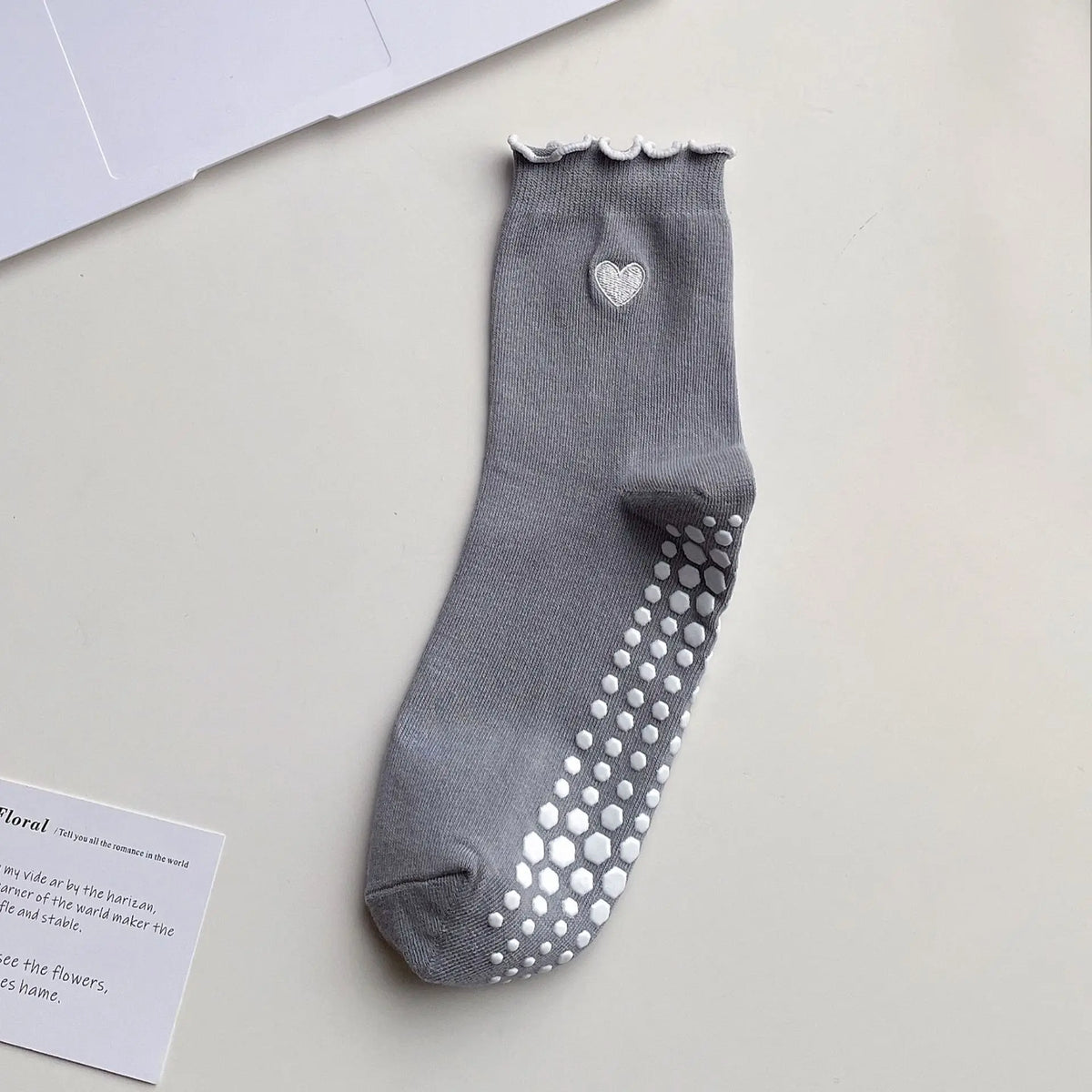 A gray yoga sock with a heart embroidery and silver studs on the toe, displayed on a white surface.