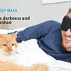 A man wearing a black sleep mask is resting in bed with an orange cat beside him.