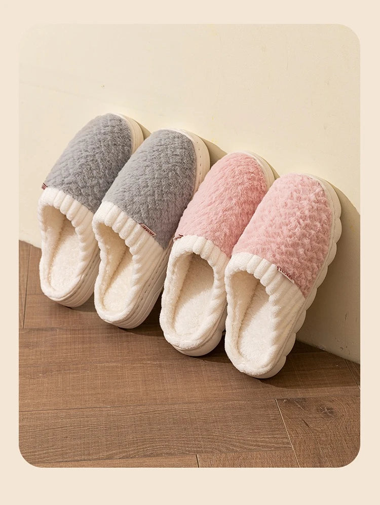 A set of four plush fleece slippers in gray, pink, and cream colors resting on a wooden floor.