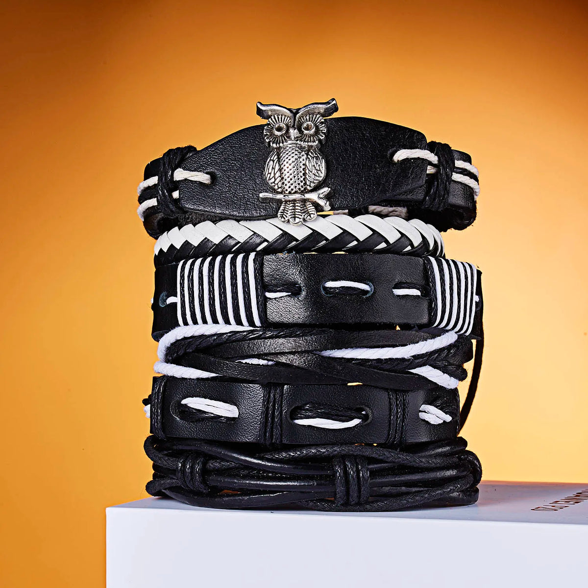 Stapel schwarzer Lederarmbänder mit Eule-Anhänger und gestreiften Designs auf weißem Untergrund