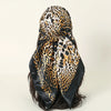 A black and gold leopard print satin square scarf tied around dark hair.