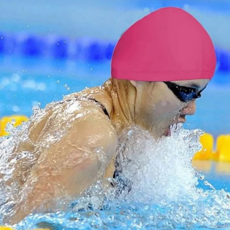Une personne portant un bonnet de bain rose éclabousse l'eau tout en nageant.