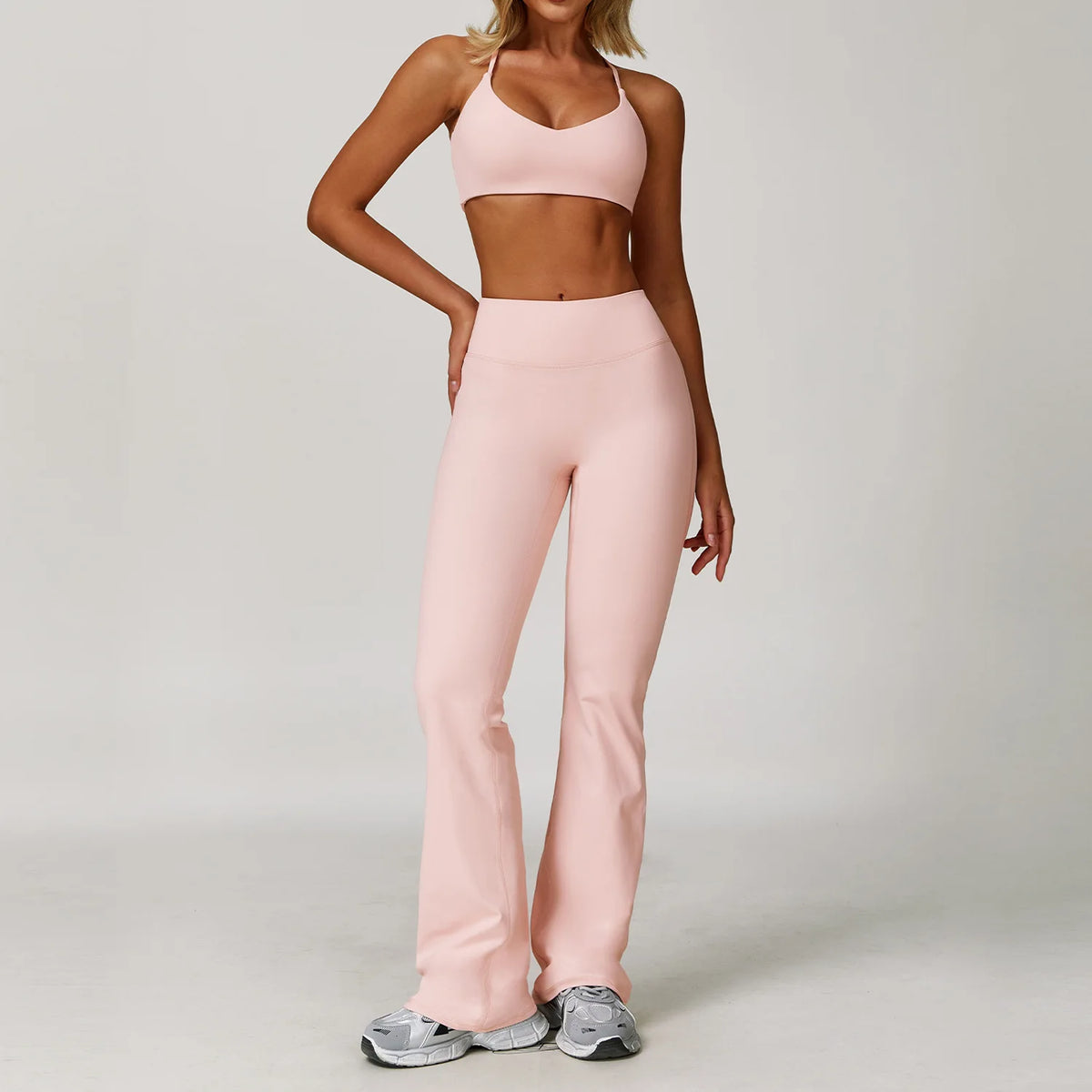 A woman wearing a light pink three-piece yoga sports set consisting of a cropped top and full-length pants.