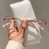 A hand holds a pair of pink cat-eye blue light blocking glasses against a white background.