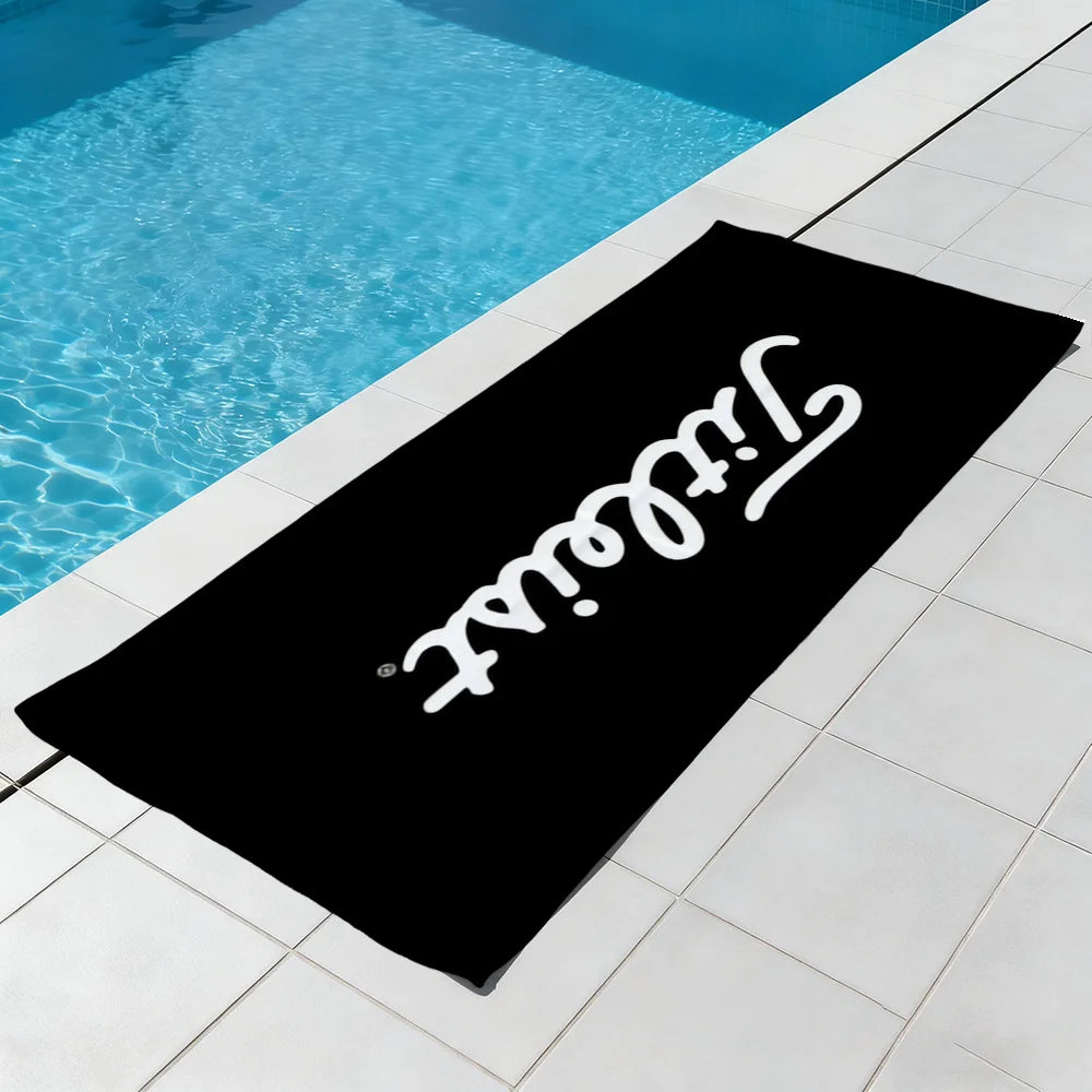 A black microfiber beach towel is laid on a tiled patio next to a swimming pool.