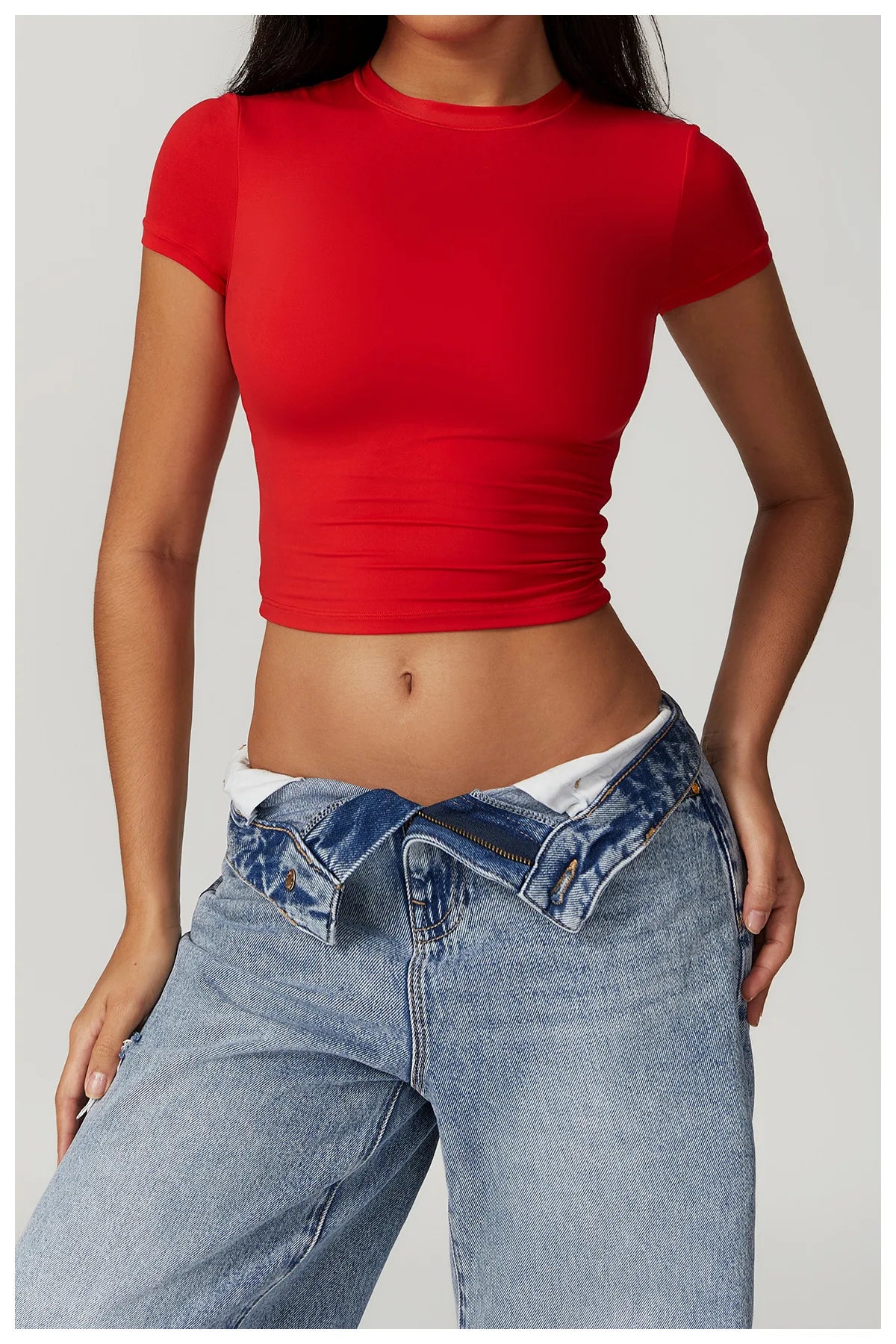 Una mujer vistiendo una camiseta deportiva roja de yoga y jeans azules.