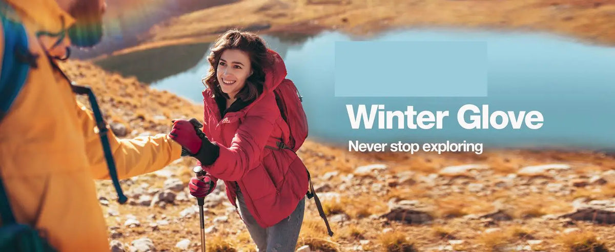 A woman wearing a red winter glove smiles while exploring outdoors in a sunny, rugged landscape.