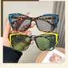 A hand holds a pair of vintage square cat eye sunglasses with tortoiseshell frames and green lenses.