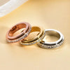 Three stacked stainless steel rings with CZ gemstones in rose gold, yellow gold, and silver tones.