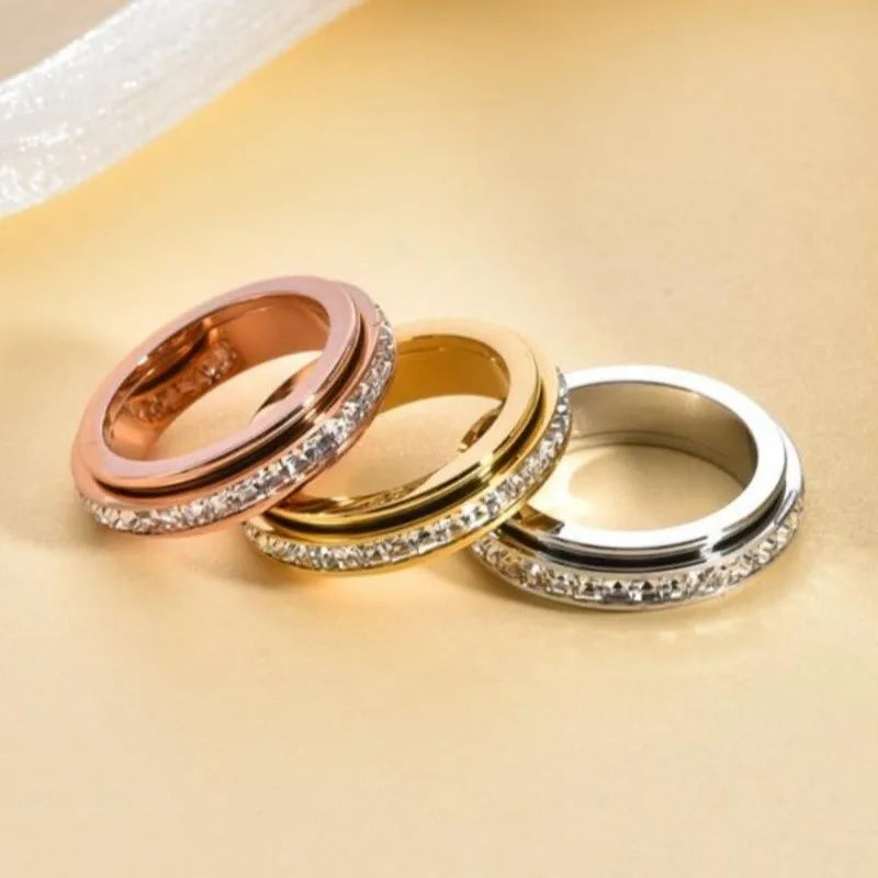 Three stacked stainless steel rings with CZ gemstones in rose gold, yellow gold, and silver tones.