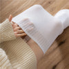 A hand is wearing a white thigh high leg warmer on its lower leg, next to a beige knitted sweater.