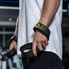 A person wearing a grey shirt is holding black gym wrist wraps with yellow lettering on their forearm.