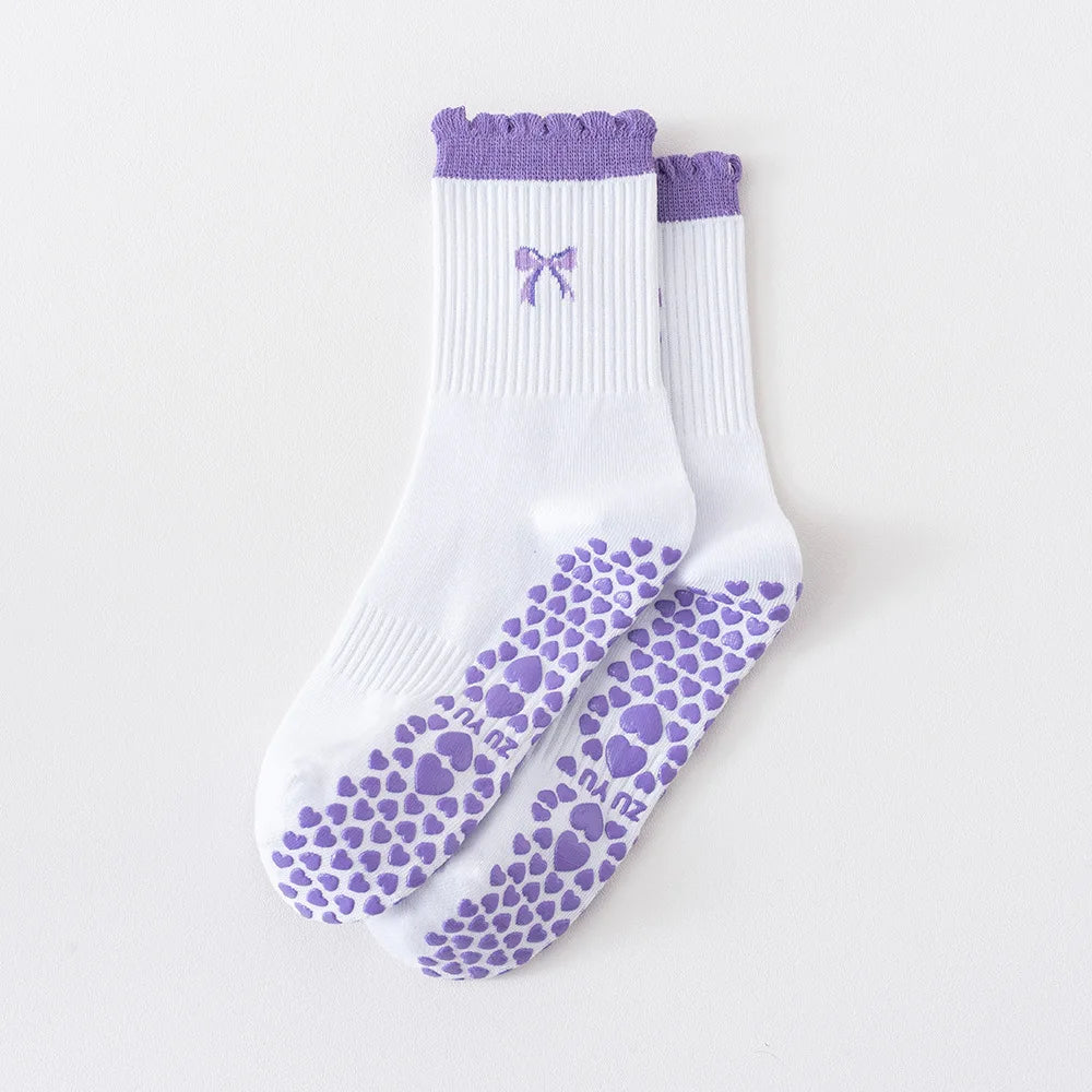 Ein Paar weiß-lila Strick-Yoga-Socken mit Schleifen- und Herzmuster auf der Sohle.
