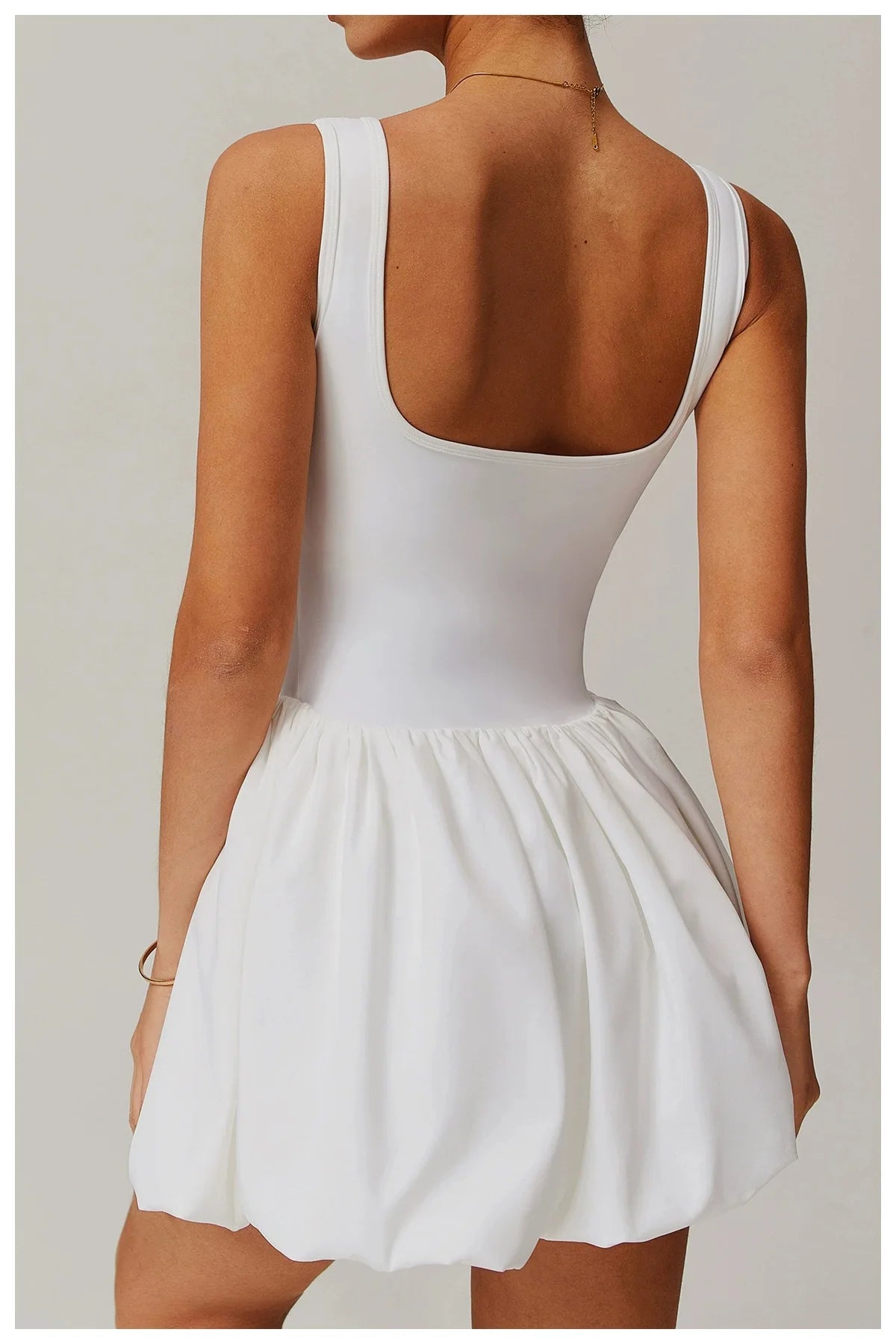 Eine Frau trägt ein weißes Performance-Tenniskleid mit ärmelloser Oberteil und plissierter Rock, von hinten gezeigt.