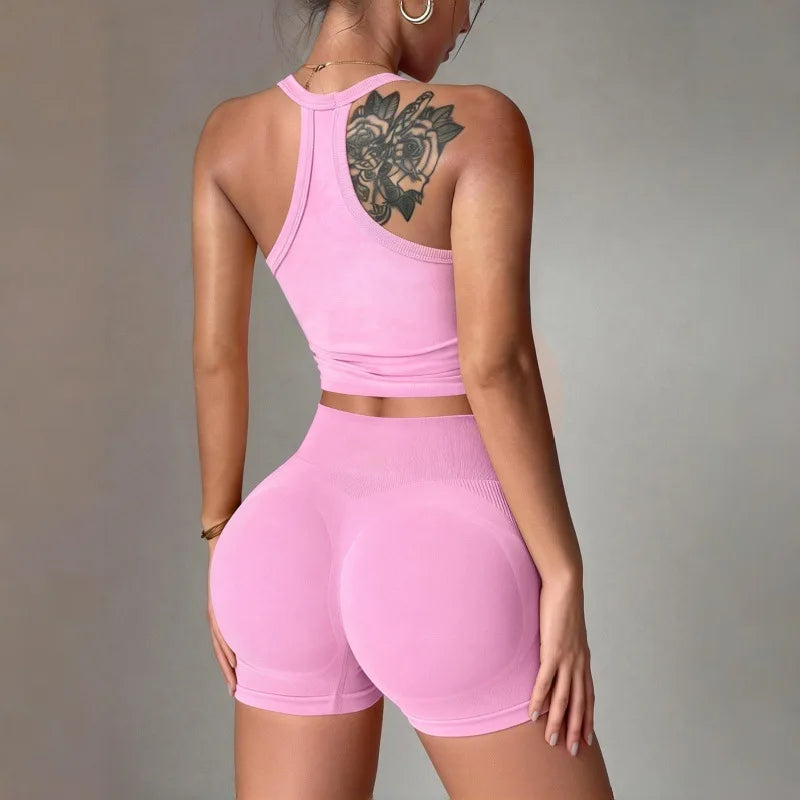 A woman models a bright pink two-piece yoga set featuring a racerback tank top and matching shorts.