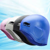 A row of five silicone swimming caps in various colors including pink, gray, black, and blue floating on a light blue backgro