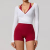 A woman models a white long sleeve top with a red V-neck and matching red yoga shorts.