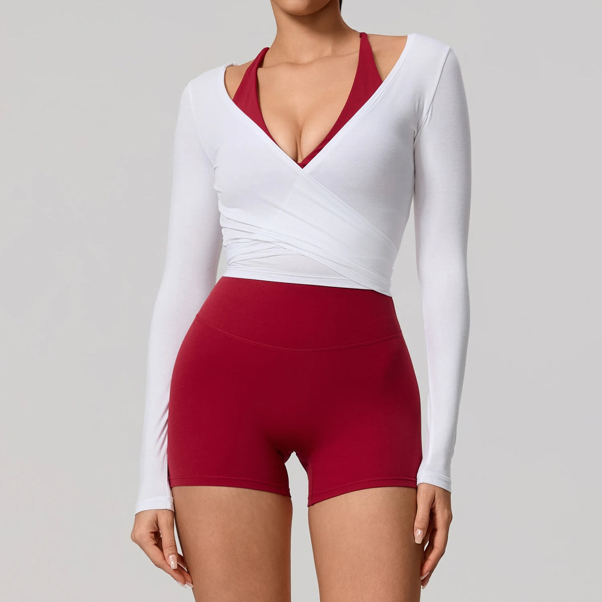 A woman models a white long sleeve top with a red V-neck and matching red yoga shorts.