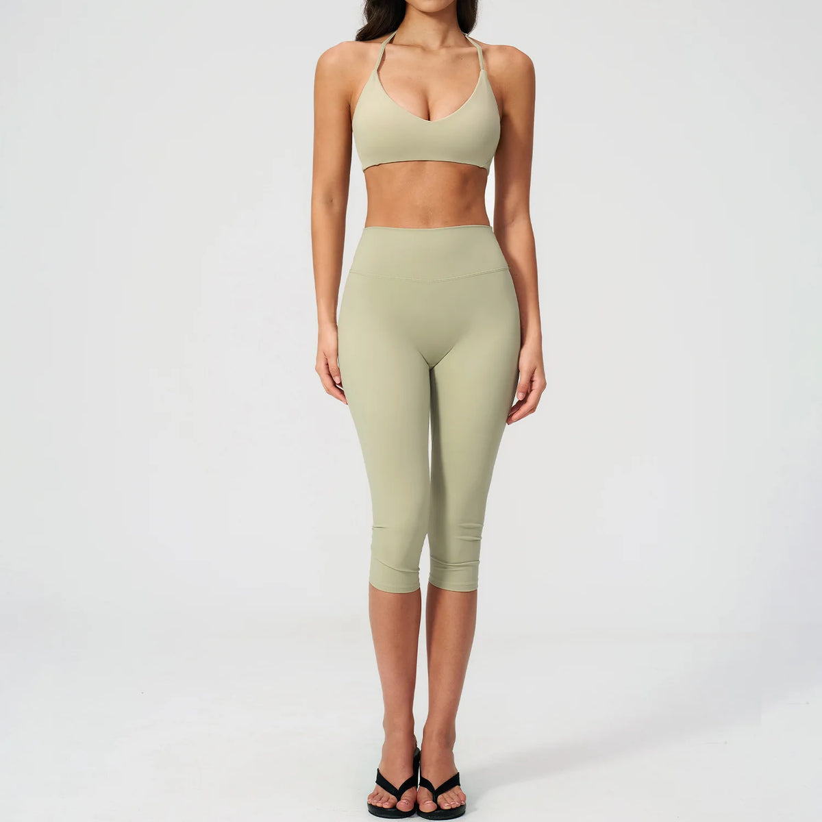 A woman models a light olive green women's premium fitness tracksuit consisting of a sports bra top and leggings.