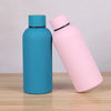 A light pink double-layer vacuum thermos cup and a teal double-layer vacuum thermos cup sitting on a wooden surface.
